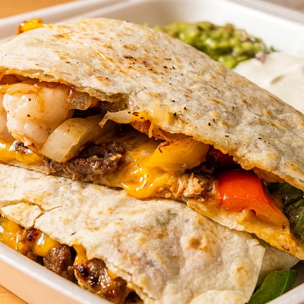 Two quesadillas filled with shrimp, steak, cheese, and vegetables, served with guacamole and lettuce.