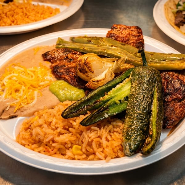 A plate of carne asada, grilled peppers, onions, refried beans with cheese, and rice.